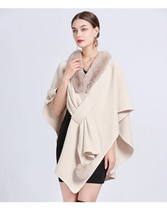 Detail of beige knit poncho featuring faux rabbit fur collar and pom-poms on the hem