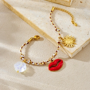 Bohemian braided rope bracelet with red lips and sun charms on a textured stone display