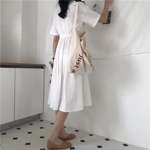 Detail view of a spacious canvas tote bag with red lettering styled with a white dress