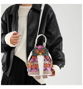 Close-up of owl-shaped shoulder bag with colorful patchwork feathers on white synthetic leather