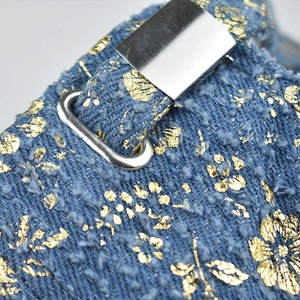 Detail of blue denim fabric with gold floral patterns and silver metal buckle hardware
