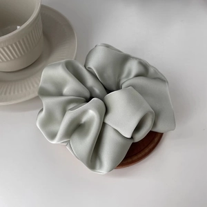 Close-up of soft light green satin silk scrunchie on a wooden tray with a white cup