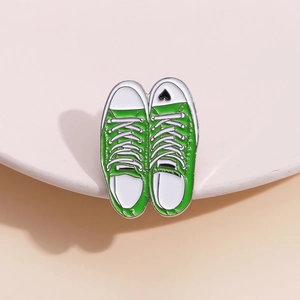 Cartoon green canvas shoe enamel pin with black heart detail on a soft pink stand