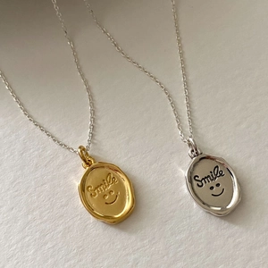 Detail showing gold and silver smile face pendant necklaces with wax seal texture