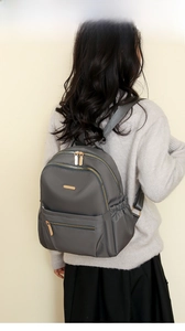 Detail showing grey nylon backpack with gold zippers and side pockets on a female model