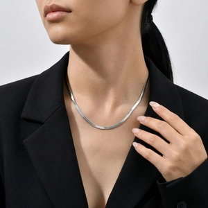 Close-up of a silver flat snake bone chain necklace worn by a model in a black suit
