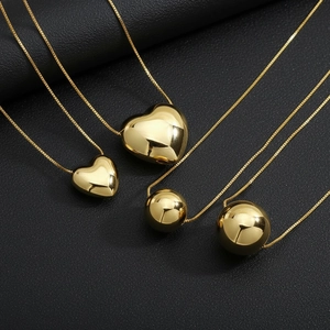Polished gold heart and ball pendants on fine box chains against black leather background