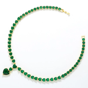 Detail of gold necklace with green heart-shaped cubic zirconia on a white surface