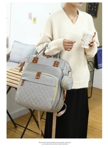 Quilted diaper backpack in grey with brown leather trim worn by model in a cafe