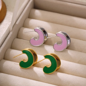 Detail of C-shaped pink and green enamel hoop earrings in a beige jewelry box