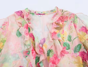 Detail of pink floral chiffon blouse featuring elegant ruffled neckline and button trim