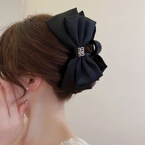 Détail d'une grande pince à cheveux avec nœud en satin noir sur une coiffure de femme