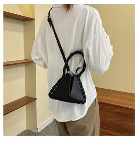Detail view of black geometric crossbody bag with woven handle on a model in a showroom
