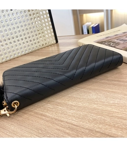 Close-up of black leather wallet with chevron stitching and golden zipper on wooden table