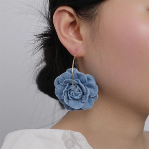 Close-up of blue denim camellia flower earrings on a model with gold metal hooks