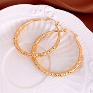 Detail of gold diamond-cut textured hoop earrings on a vintage porcelain plate background