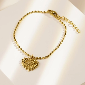 Golden beaded bracelet with heart-shaped evil eye pendant on a white background