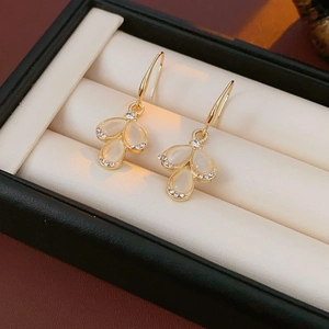 Close-up of golden teardrop earrings with opal and sparkling rhinestones in a gift box
