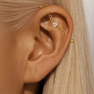 Detail of gold industrial piercing featuring a chain and white crystal flower embellishment