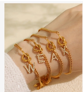 Nahaufnahme goldener Buchstaben-Armbänder W, E, A, K mit Strassbesatz und Knotenverschluss