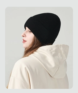 Detail einer schwarzen Grobstrickmütze an einem Modell mit grauem Kapuzenpullover