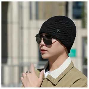 Detail of black knit beanie featuring a ribbed texture and metallic logo emblem