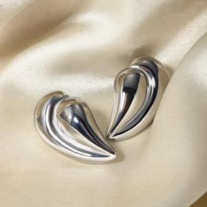 Macro view of silver streamline ear cuffs on beige silk cloth with mirror finish