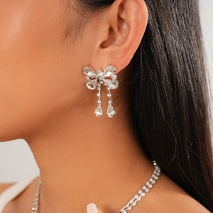 Close-up of silver bow earrings with sparkling rhinestones and drop tassel on model