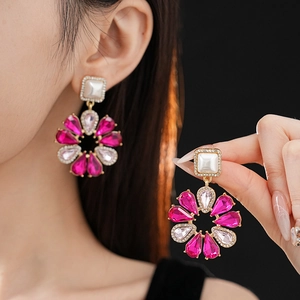 Dettaglio di orecchini a fiore dorati con pietre rosa e perle indossati da modella