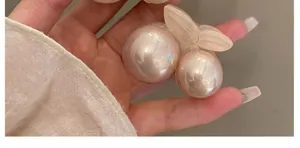 Detail of a cherry hair clip with pink pearl texture and cream leaves held by hand