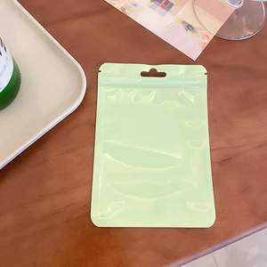 Macro detail of a green resealable ziplock pouch with a hanging hole on a wooden desk