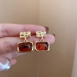 Detail of gold irregular textured metal earrings with square amber resin pendants