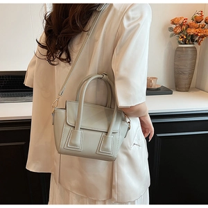 Minimalist beige bucket bag worn as a shoulder bag in an elegant indoor setting