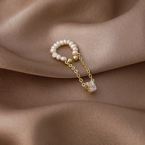 Detail of pearl ear cuff with gold tassels and a square zircon on brown silk fabric