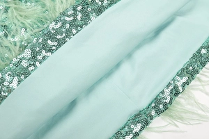 Macro detail of mint green sequins and fluffy feather trim on a fitted party dress