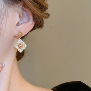 Gros plan détaillé d'une boucle d'oreille fleur plaquée or avec zircons portée par un mannequin