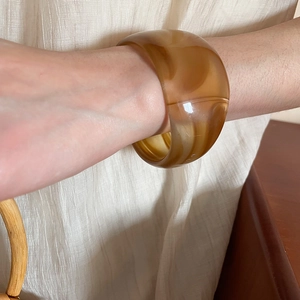 Close-up of a wide translucent amber resin bangle bracelet on a woman's wrist