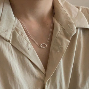 Detail of a silver oval multilayer pendant necklace worn on a neck with a beige shirt