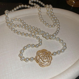 Détail d'un collier de perles orné d'un pendentif rose doré serti de cristaux étincelants