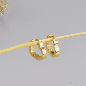 Detailed view of heart-shaped gold hoop earrings hanging on a thin decorative branch