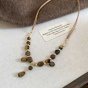 Detail of tiger eye beaded necklace with brown woven cord and gold metal accents