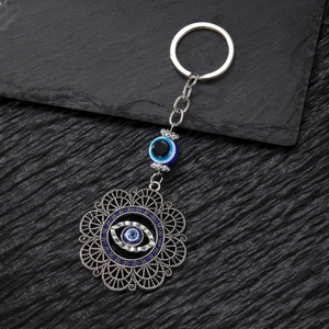 Detailed view of silver evil eye and hollow hamsa hand keychain on dark stone
