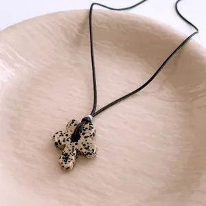 Retro wax rope necklace with flower-shaped dalmatian stone pendant on ceramic tray