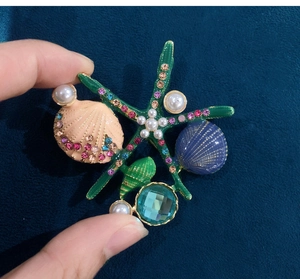 Macro shot of colorful enamel starfish and shell brooch with pearls on blue velvet
