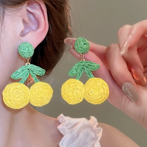 Macro detail of yellow woven cherry earrings with green leaves worn on model's ear