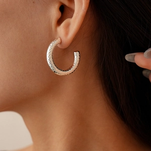 Detailed close-up of C-shaped silver earrings with textured hammered finish on a model