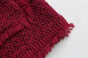 Primer plano de tejido de punto rojo oscuro con bordes de flecos e hilos brillantes