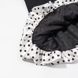 Detailed view of black silk-like hem with white polka dot ruffles and soft texture