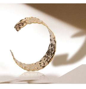 Macro detail of wide gold cuff bracelet featuring unique hammered texture and reflections