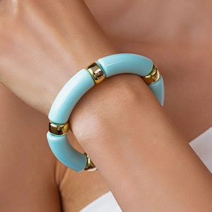 Dettaglio del bracciale in acrilico blu con perline in metallo dorato sul polso